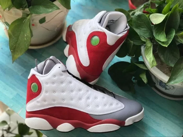 Red, white, and gray basketball shoes with green accents, displayed outdoors