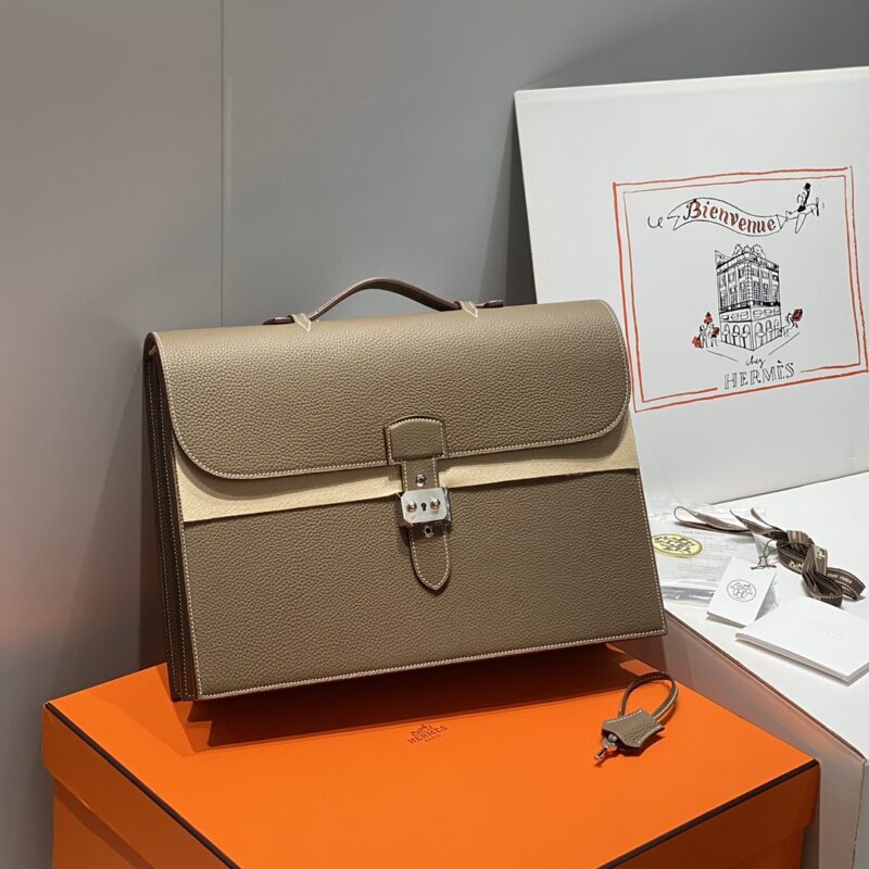 Grey leather handbag with silver metal buckle, displayed on an orange box