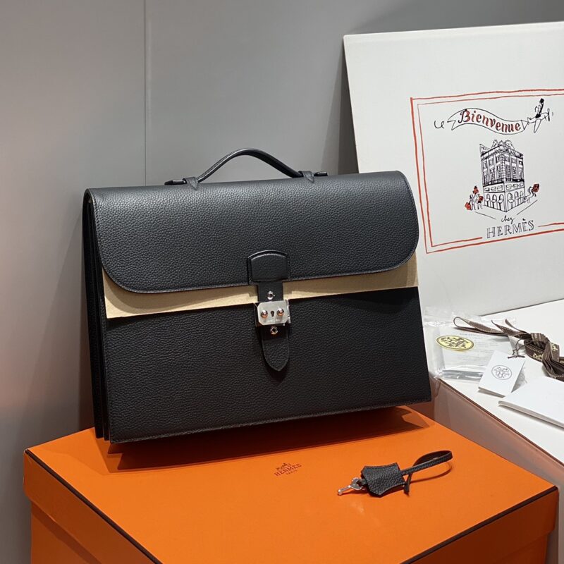 Black leather handbag with silver metal buckle, displayed on an orange box